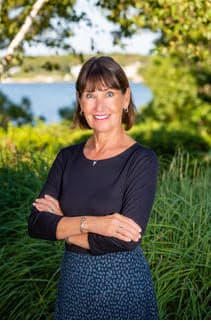 Michelle Lawton, smiling, arms folded, outdoors with the water behind her